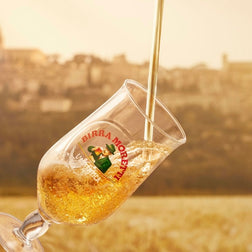 Wine glass with logo being filled, blurred background of hills and sky.