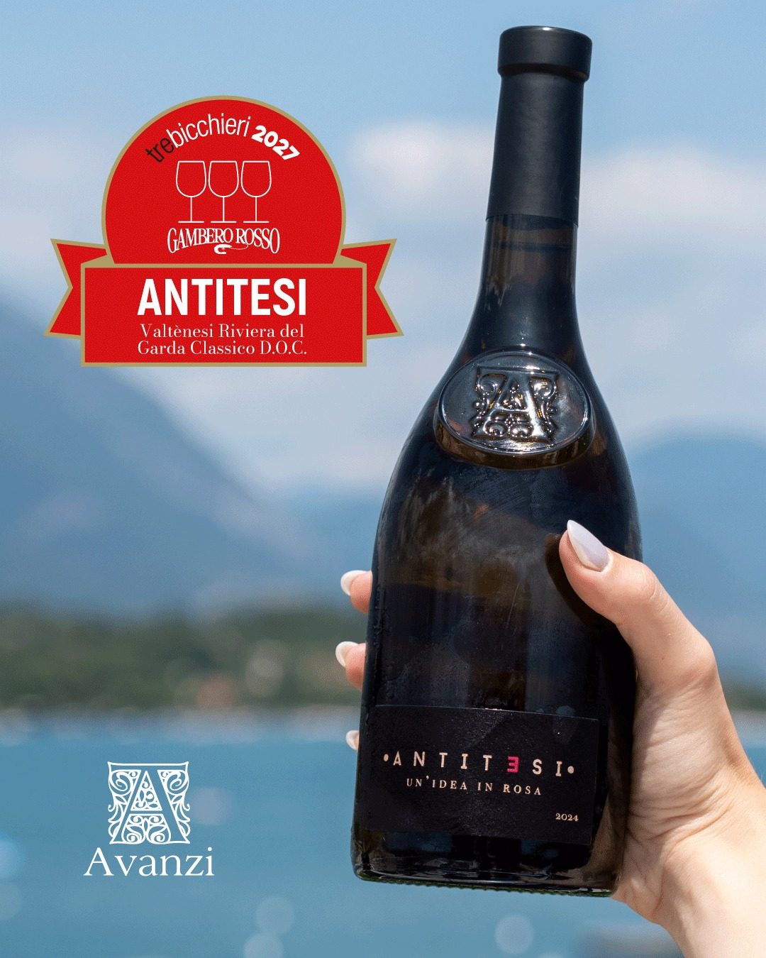 A bottle of Antitesi 2024 held up against Lake Garda, with the Gambero Rosso Tre Bicchieri 2027 badge